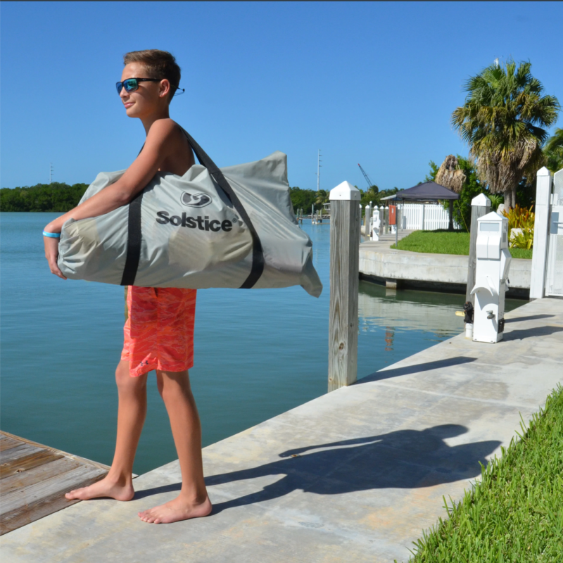 Young man carrying Solstice 6x5 Inflatable Dock in carrying bag.