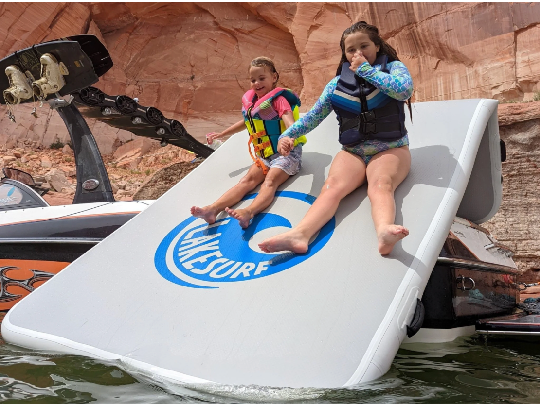 Two kids sliding  down the Slide Island Inflatable slide dock by Lakesurf